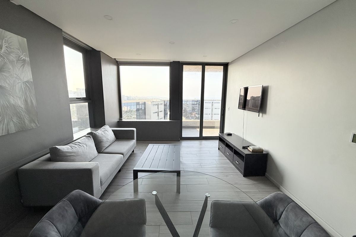 Modern living room featuring large format floor tiles, recessed downlighting, and expansive windows providing natural light and access to a private balcony.