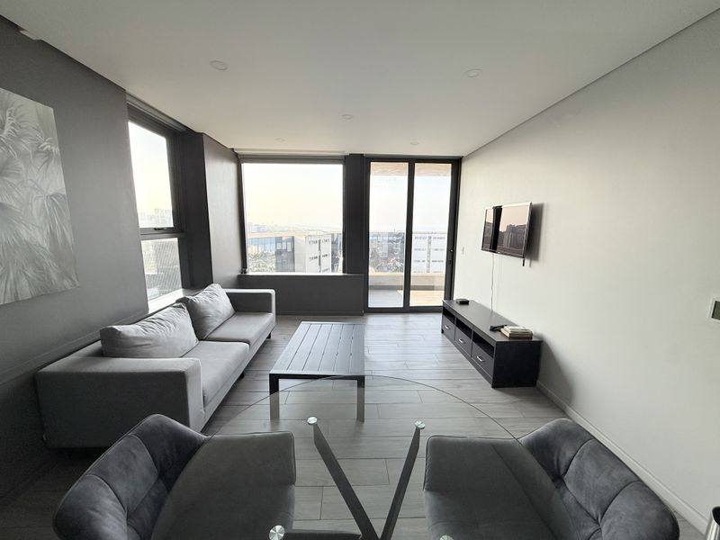 Modern living room featuring large format floor tiles, recessed downlighting, and expansive windows providing natural light and access to a private balcony.