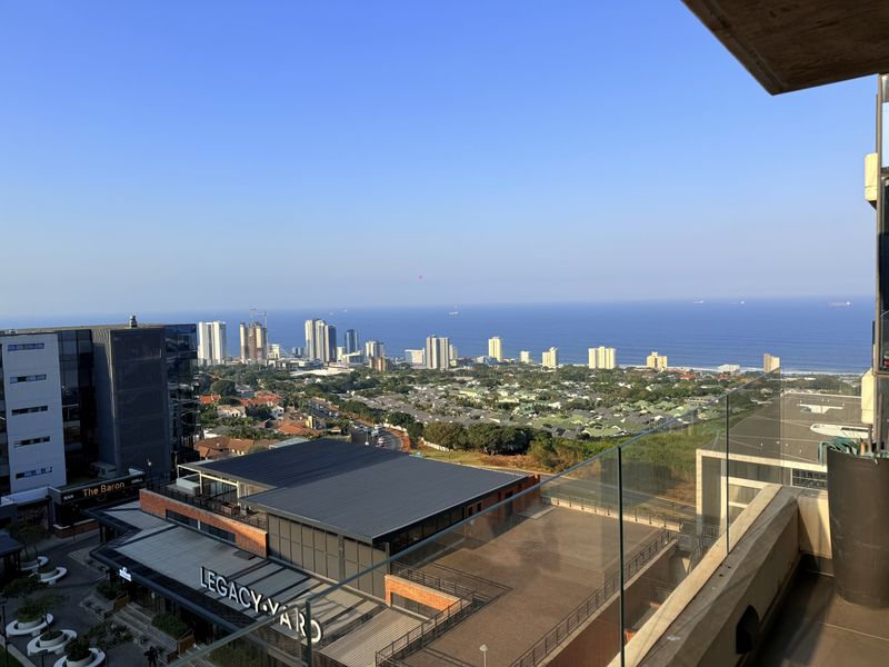 Elevated panoramic view overlooking the coastal urban landscape and ocean, captured from a balcony with a modern glass balustrade.