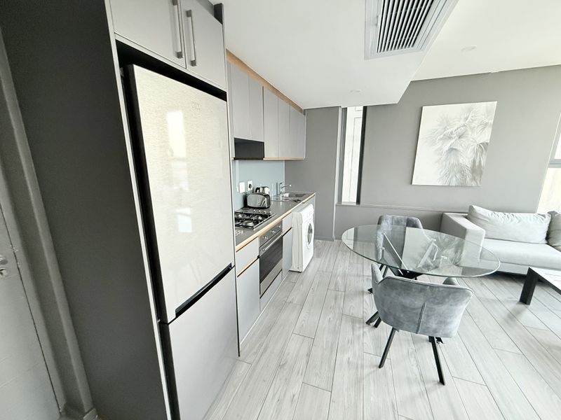 Modern open-plan apartment featuring a sleek kitchen with built-in appliances, integrated laundry, and contemporary tiled flooring, seamlessly flowing into the living and dining area.
