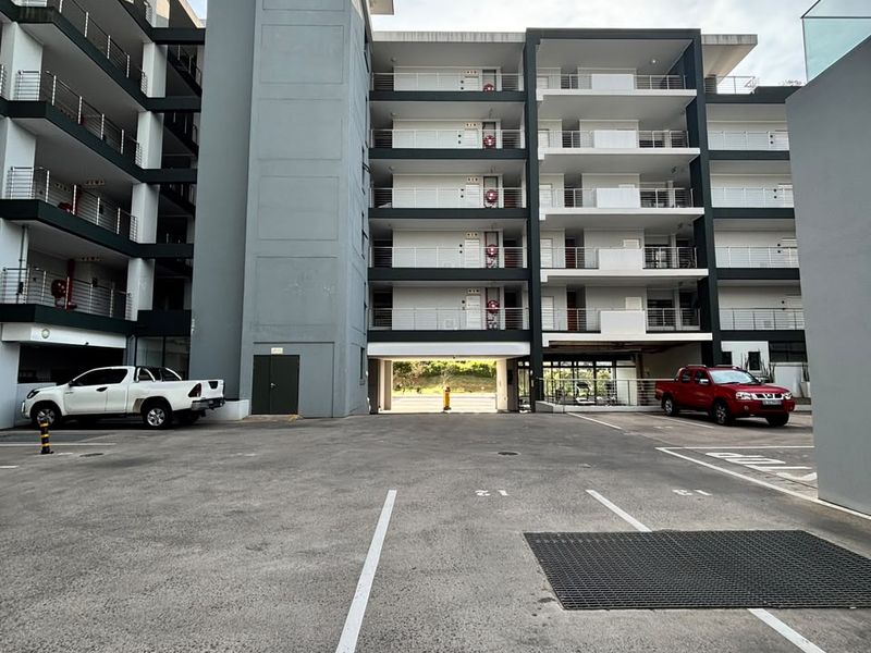 Exterior view of a modern multi-story apartment complex featuring a paved parking area and balconies with metal railings.