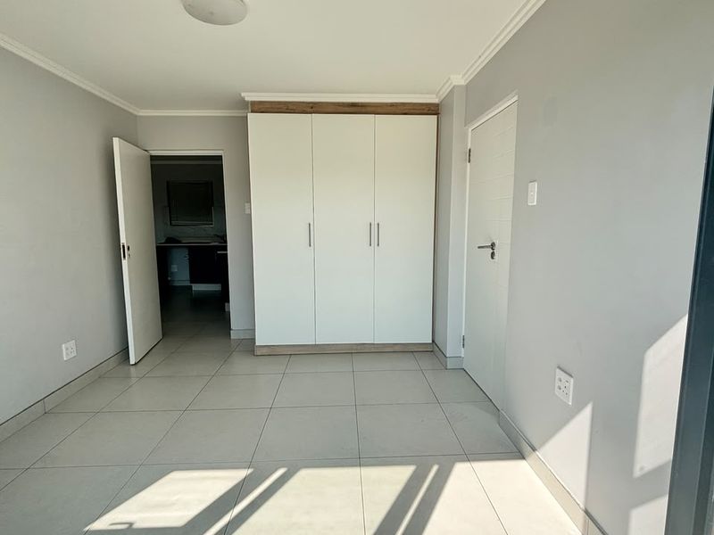 A bright, empty bedroom featuring neutral tiled flooring, a modern built-in wardrobe, and clean finishes, ready for personalization.