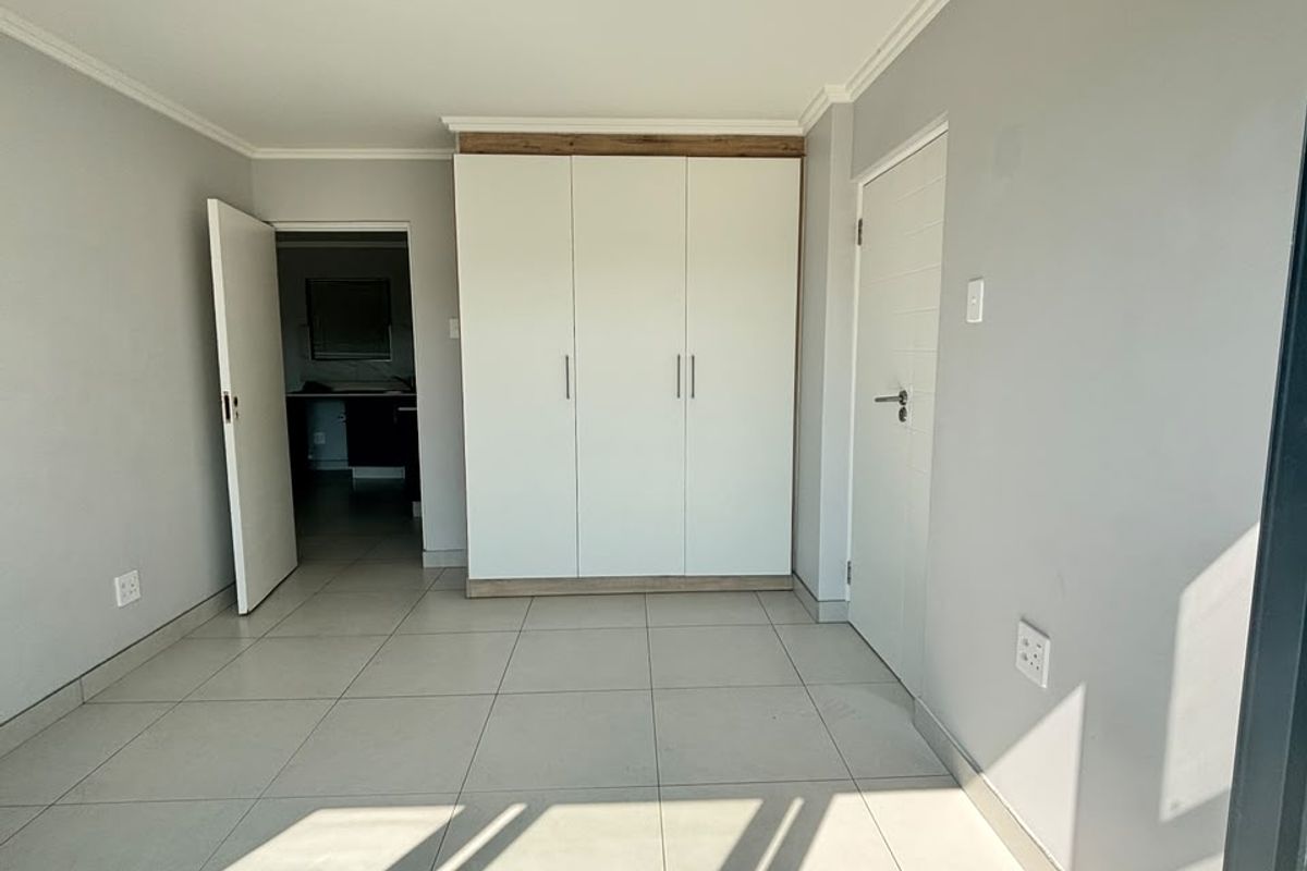 A bright, empty bedroom featuring neutral tiled flooring, a modern built-in wardrobe, and clean finishes, ready for personalization.