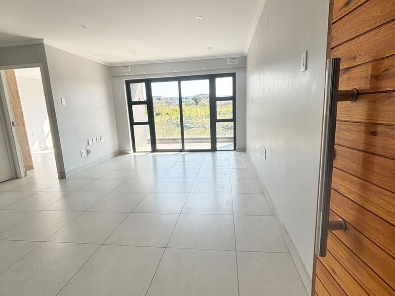 A bright, empty living area featuring large sliding glass doors, neutral tiled flooring, and a modern timber entrance door.