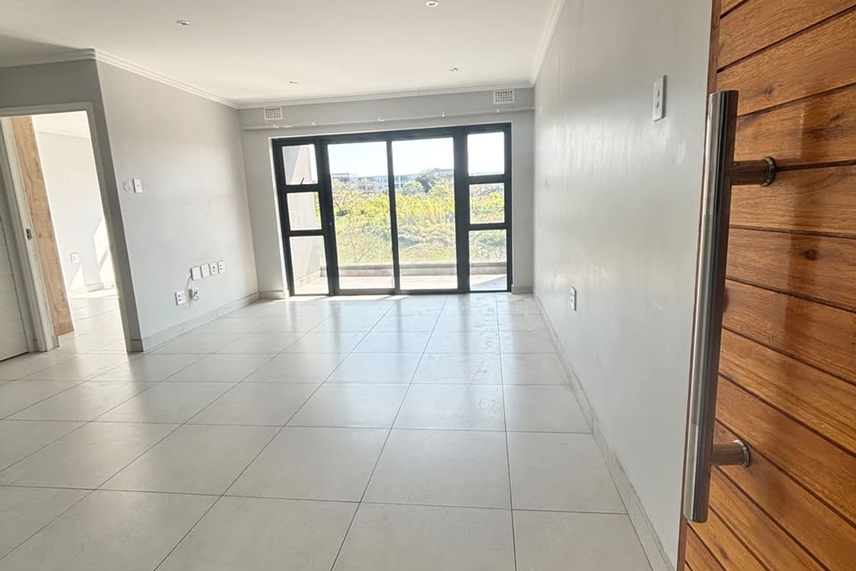 A bright, empty living area featuring large sliding glass doors, neutral tiled flooring, and a modern timber entrance door.