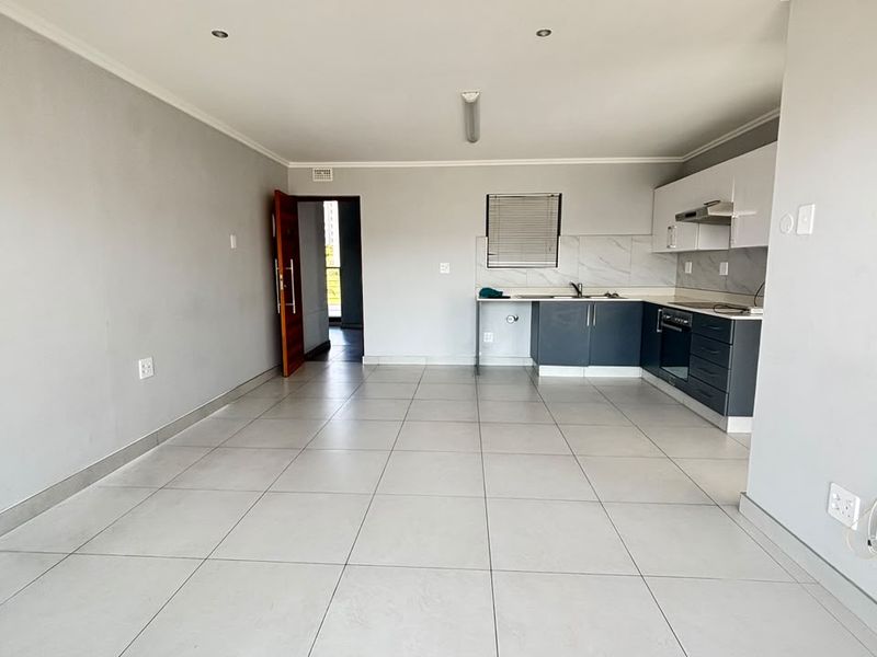 An open-plan living and kitchen area featuring modern grey cabinetry, tiled floors, and neutral walls, offering a clean and versatile space.