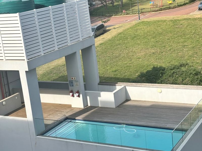 Elevated outdoor pool area featuring timber decking, glass balustrades, and integrated water storage tanks overlooking the complex grounds.