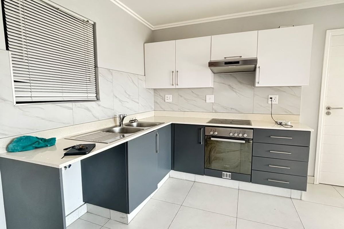 Modern kitchen featuring two-tone cabinetry, marble-look backsplash, quartz countertops, built-in oven, hob, and extractor fan with neutral tiled flooring.