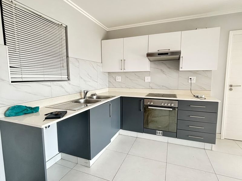Modern kitchen featuring two-tone cabinetry, marble-look backsplash, quartz countertops, built-in oven, hob, and extractor fan with neutral tiled flooring.