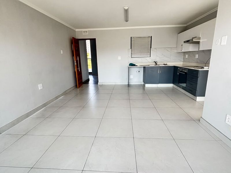 Spacious open-plan living area featuring large format floor tiles, recessed lighting, and a modern kitchen with built-in cabinetry and integrated appliances.