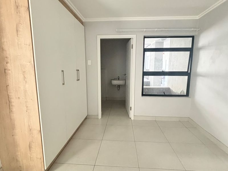 A bright, empty bedroom featuring neutral tiled flooring, a modern built-in wardrobe with wood-grain accents, and an en-suite bathroom access.