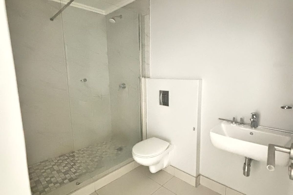 A modern, clean bathroom featuring a walk-in shower with glass screen, wall-mounted toilet, and a wall-mounted basin with neutral floor tiling.