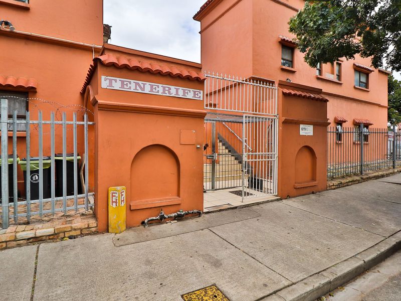 Front entrance view of the Tenerife apartment complex featuring a secure metal gate, terracotta roof detailing, and concrete sidewalk access.