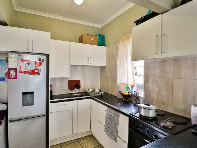 A functional kitchen featuring white built-in cabinetry, dark laminate countertops, a stainless steel sink, and an integrated electric stove with tiled backsplash.