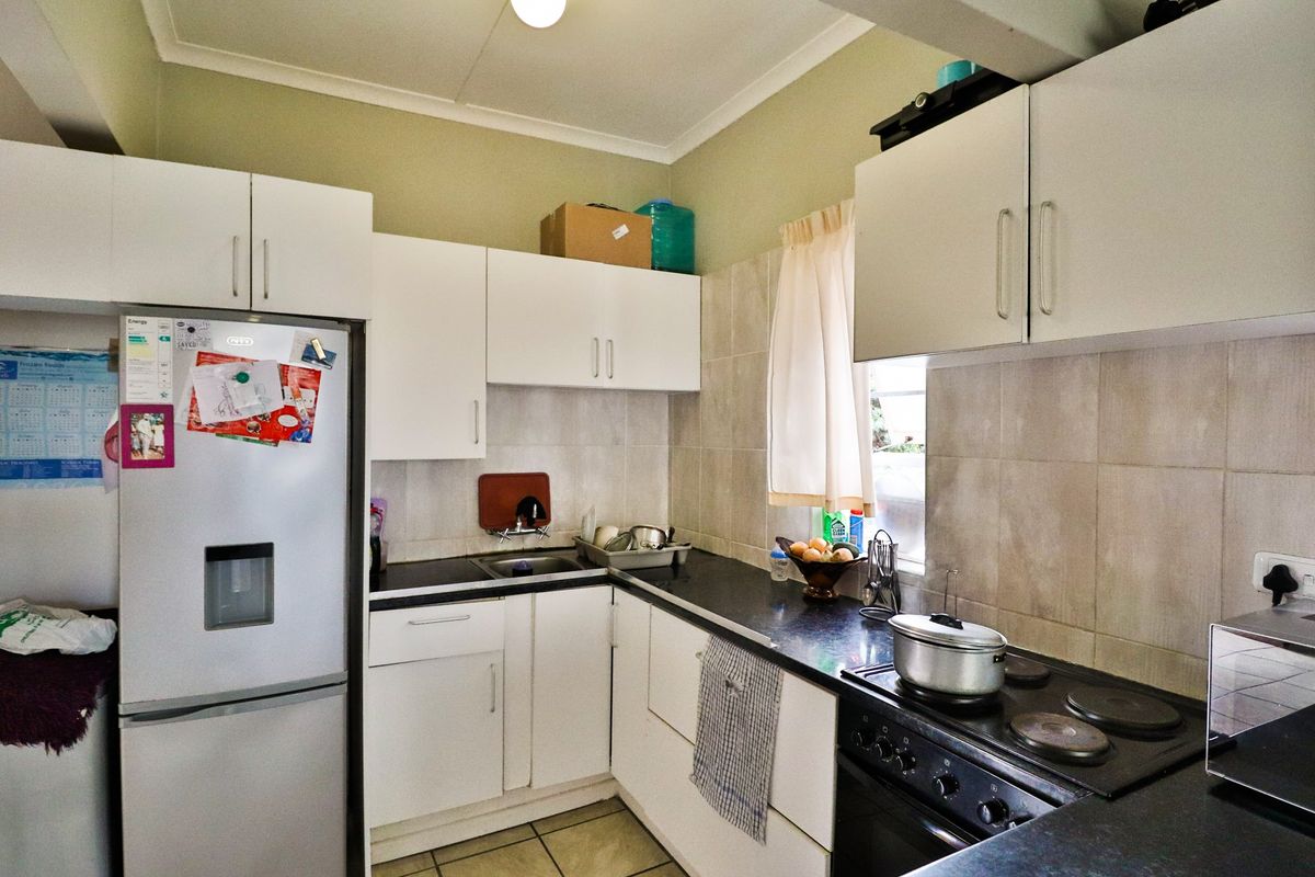 A functional kitchen featuring white built-in cabinetry, dark laminate countertops, a stainless steel sink, and an integrated electric stove with tiled backsplash.