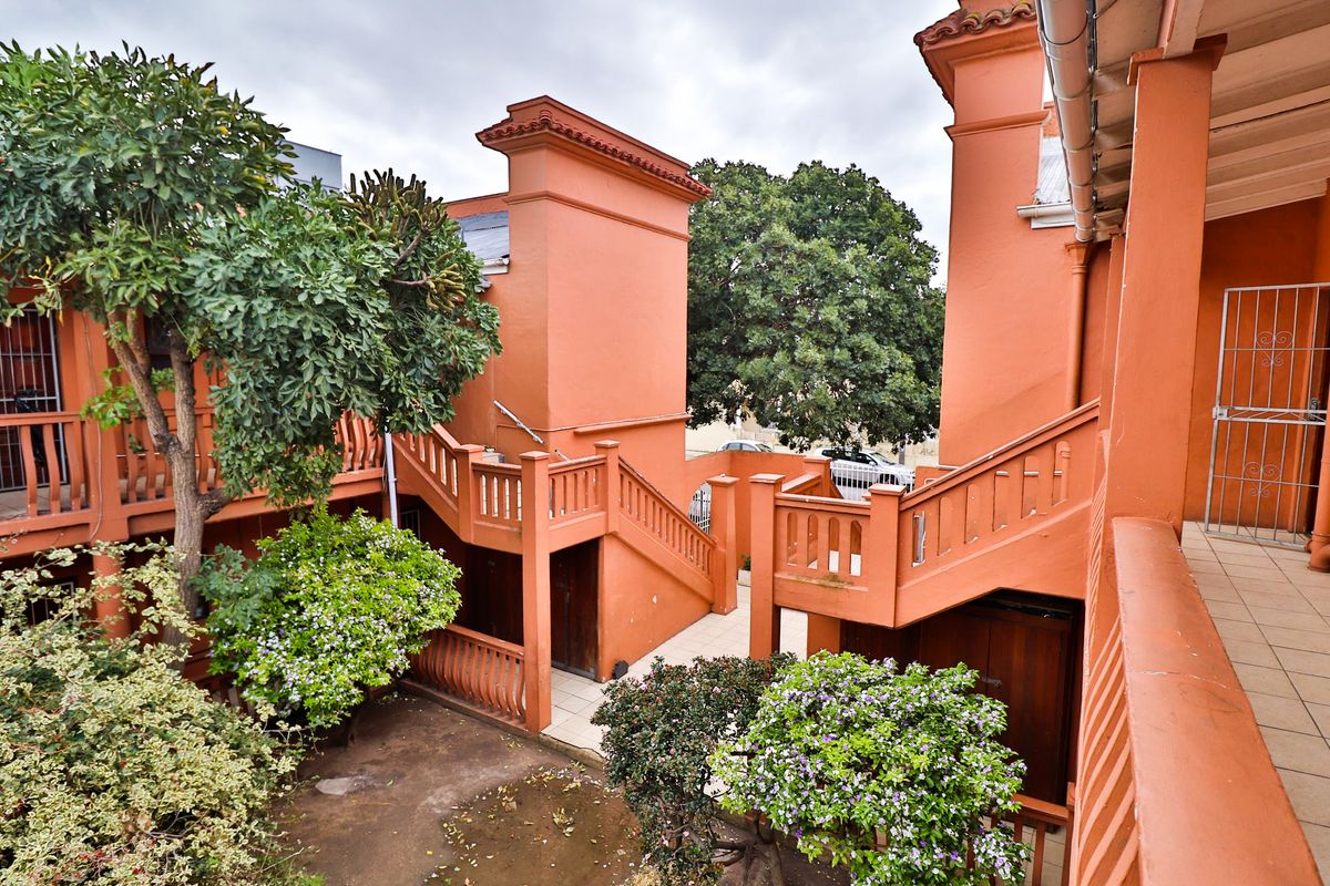 An exterior view of an apartment complex courtyard featuring terracotta-colored staircases, balustrades, and paved walkways surrounded by established greenery.