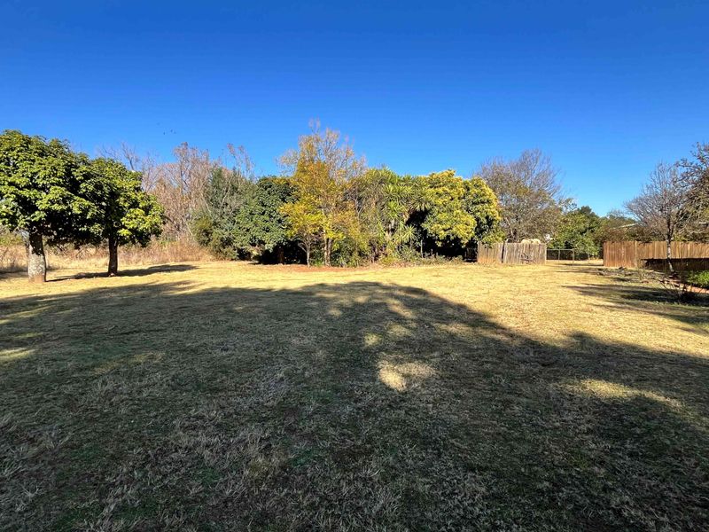 A spacious, open garden area featuring established trees and perimeter wooden fencing, offering a natural and private outdoor setting.