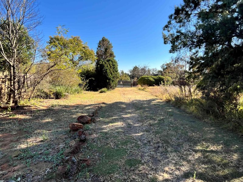 A view of the property grounds featuring a long driveway leading to a metal entrance gate, surrounded by mature trees and natural landscaping.