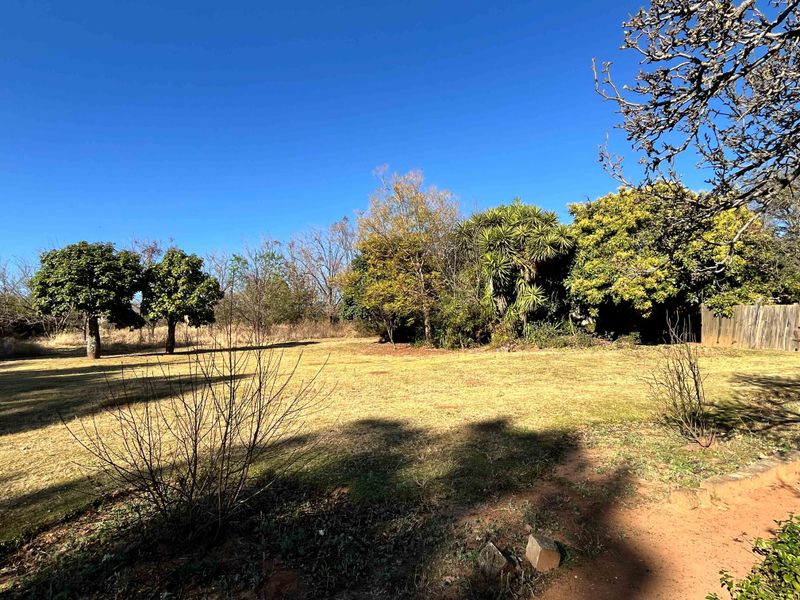 A spacious, open garden area featuring mature trees and a wooden boundary fence on a small holding property.