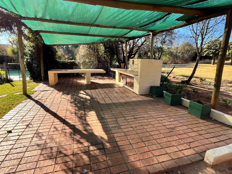 Outdoor patio area featuring brick paving, a built-in braai station, and a shaded canopy structure overlooking the garden.