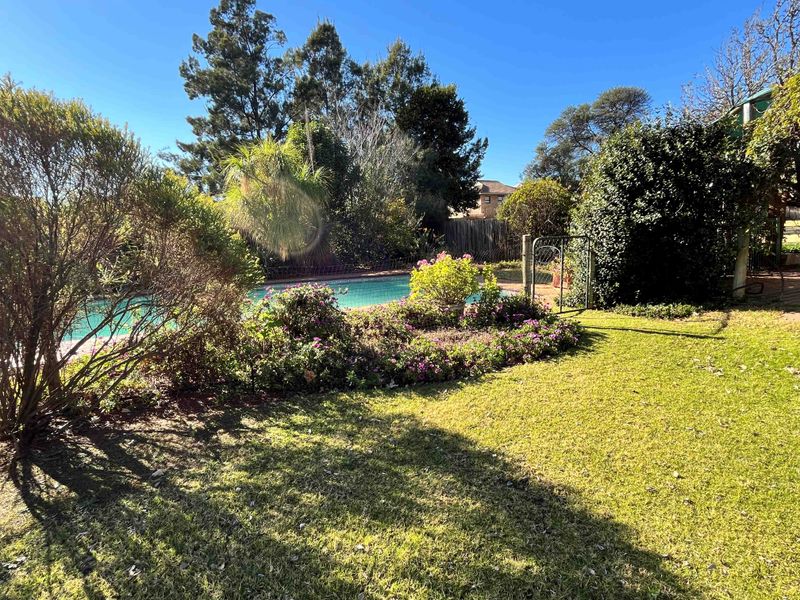 A private outdoor pool area featuring a swimming pool, safety fencing, and established garden landscaping on a small holding property.