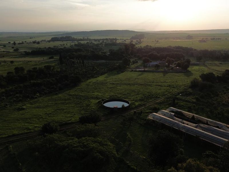Aerial view of the farm property featuring a circular water reservoir, greenhouse structures, and expansive open grazing land at sunset.