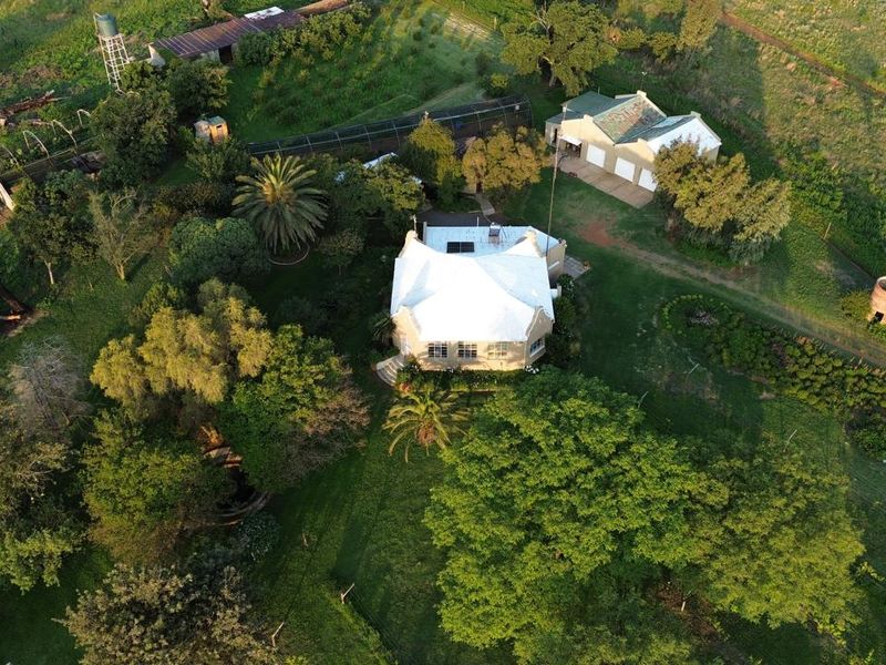 Aerial view of a farm property featuring a main residence with a metal roof, surrounding gardens, outbuildings, a garage, and a windmill.