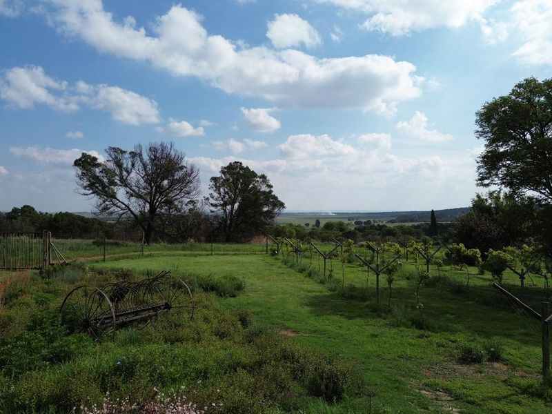 Expansive farm garden featuring a trellis system, open green space, and perimeter fencing with scenic rural landscape views.