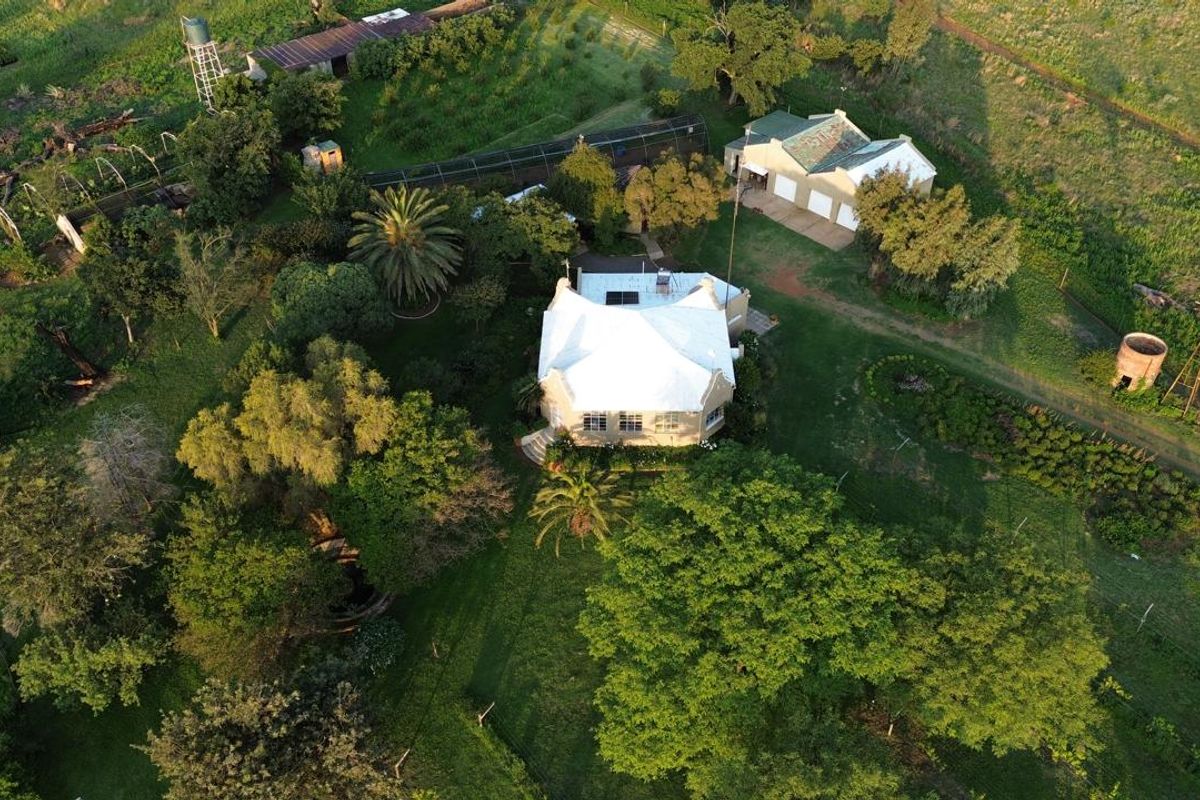Aerial view of a farm property featuring a main residence with a metal roof, surrounding gardens, outbuildings, a garage, and a windmill.