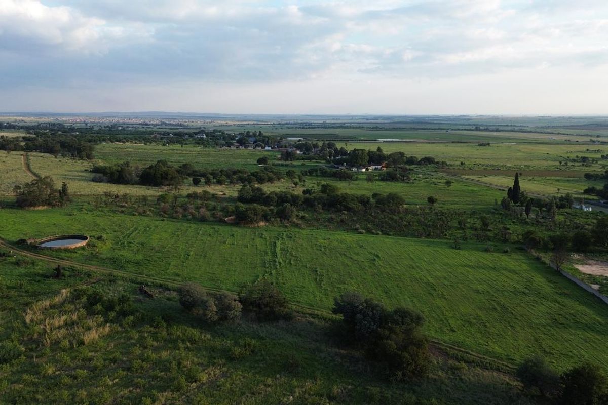 An aerial view of the expansive farm property, showcasing open green pastures, natural landscape, and existing water infrastructure.