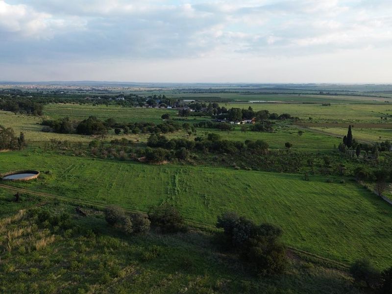 An aerial view of the expansive farm property, showcasing open green pastures, natural landscape, and existing water infrastructure.