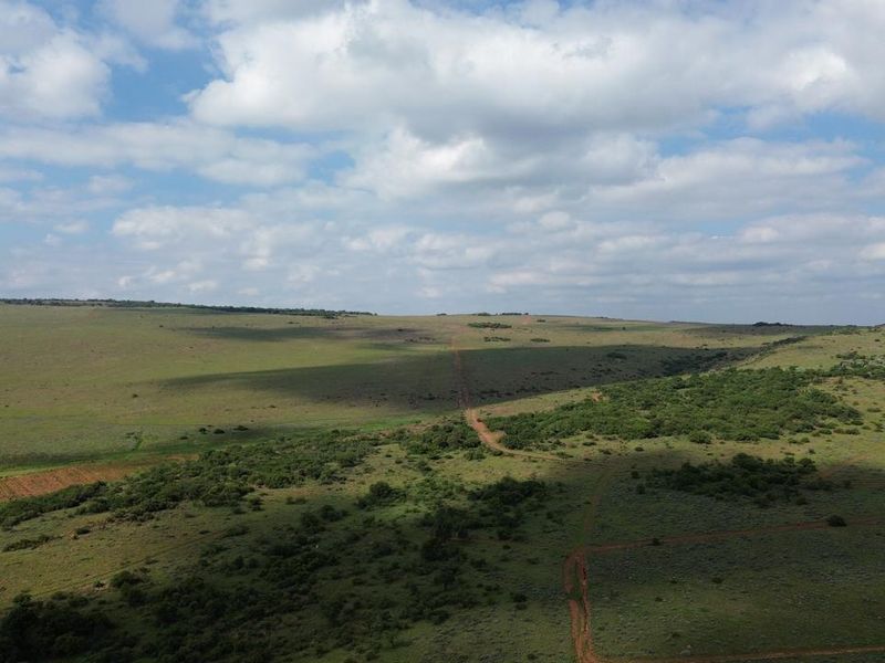 An aerial view of the expansive farm landscape featuring rolling hills, natural vegetation, and a dirt access track.