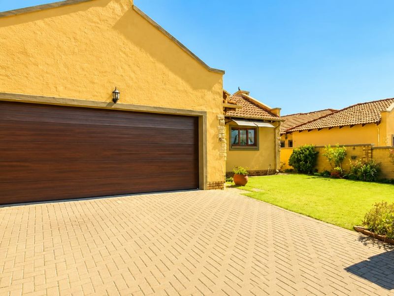 Front view of the property featuring a paved driveway, a double garage with a modern door, and a well-maintained garden area.