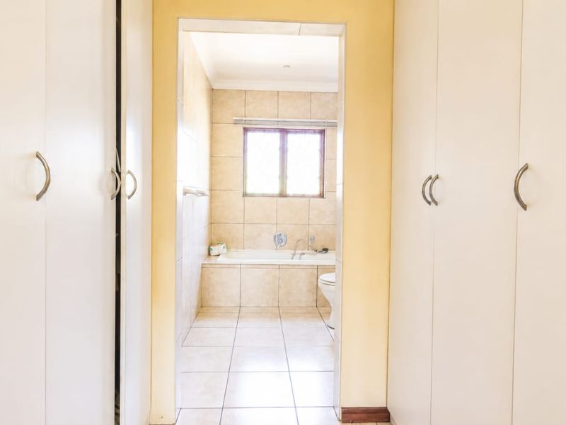 A bathroom accessed through a dressing area with built-in cupboards, featuring tiled finishes, a bathtub, and a toilet.