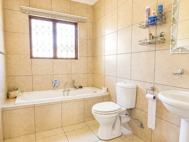 A functional bathroom featuring a built-in bathtub, pedestal sink, toilet, and neutral ceramic tiling throughout.