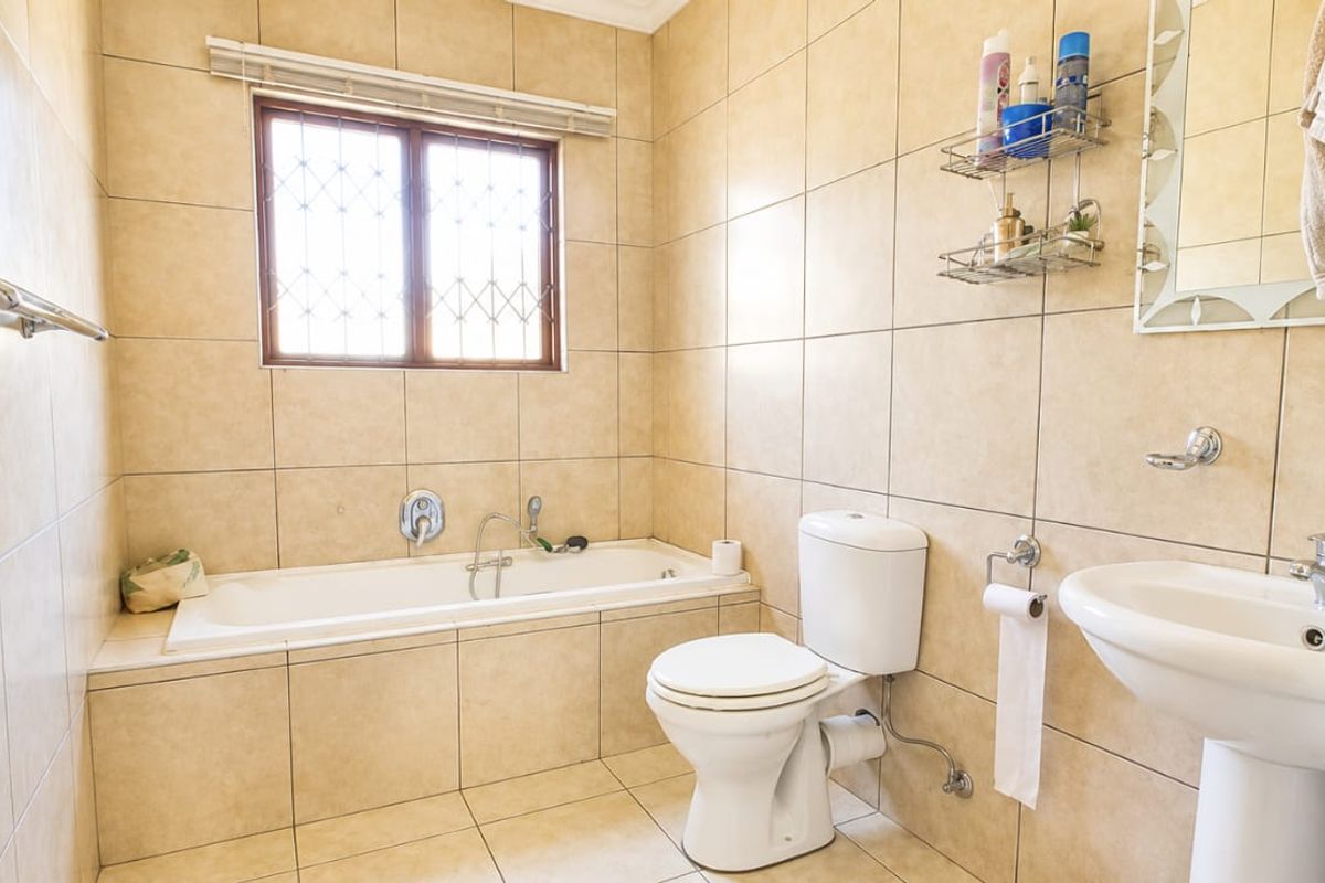 A functional bathroom featuring a built-in bathtub, pedestal sink, toilet, and neutral ceramic tiling throughout.