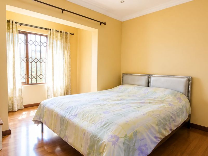 A well-lit bedroom featuring laminate flooring, security bars on the window, and classic cove cornice detailing.