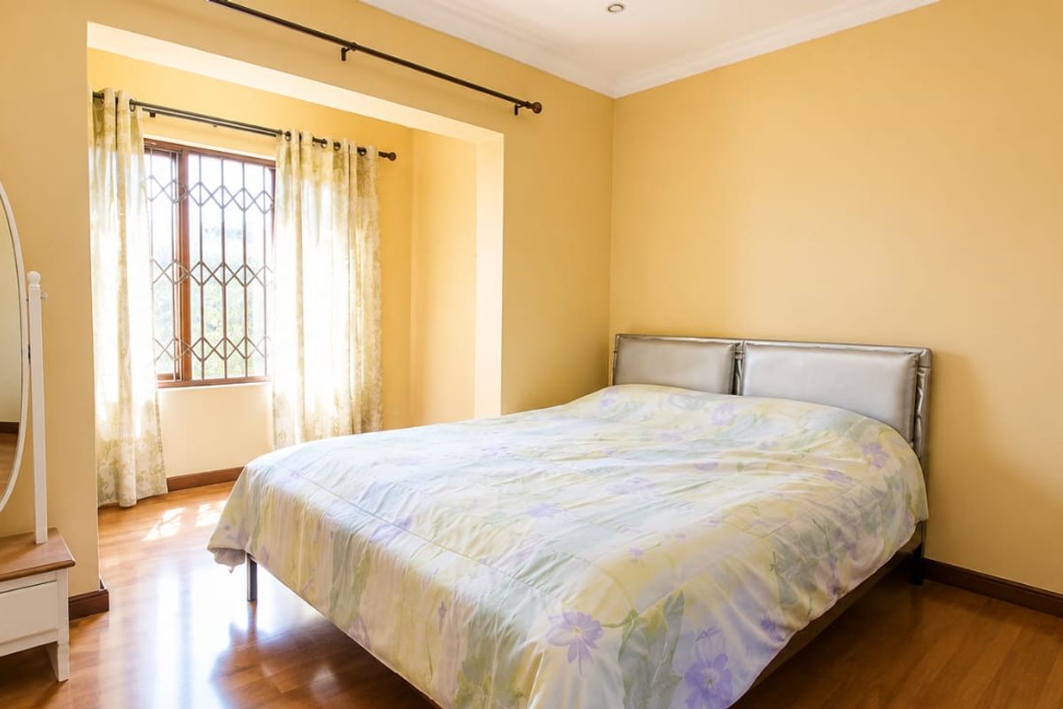 A well-lit bedroom featuring laminate flooring, security bars on the window, and classic cove cornice detailing.