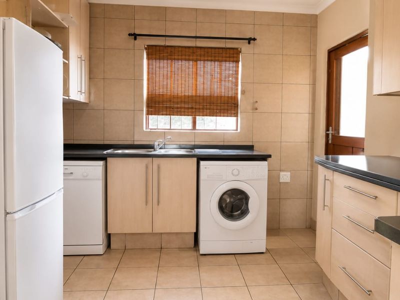 Functional kitchen featuring light wood-look cabinetry, dark countertops, tiled splashbacks, and dedicated spaces for laundry and kitchen appliances.