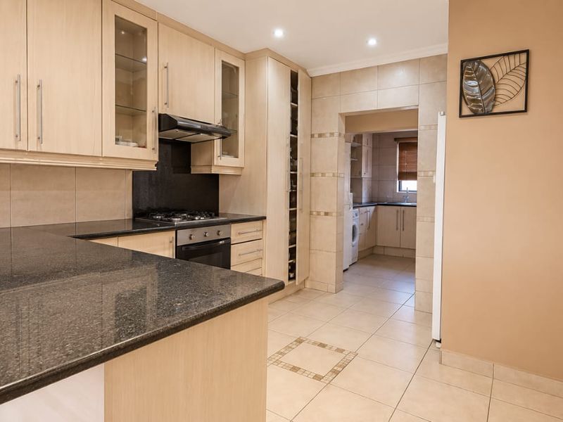 A well-maintained kitchen featuring granite countertops, built-in cabinetry, a gas hob, and an integrated oven, with an adjacent scullery area.