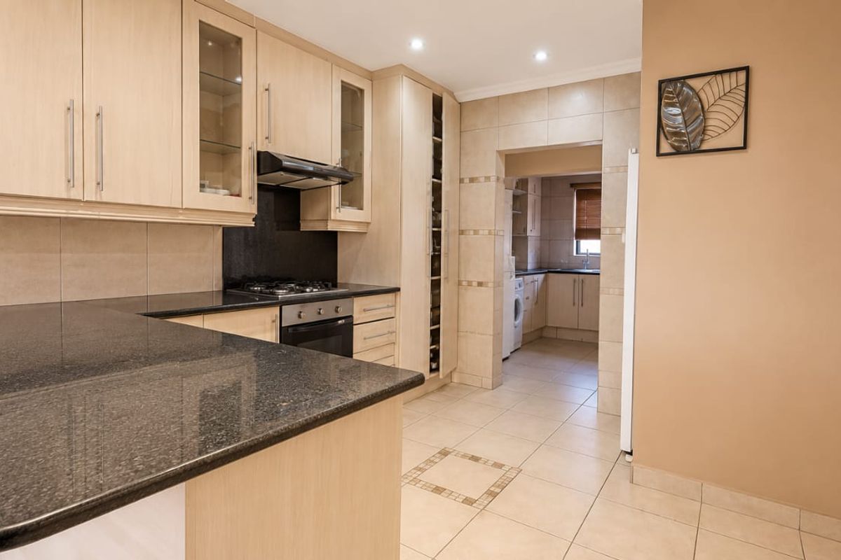 A well-maintained kitchen featuring granite countertops, built-in cabinetry, a gas hob, and an integrated oven, with an adjacent scullery area.
