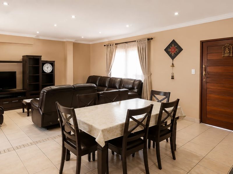 Spacious open-plan living and dining area featuring tiled flooring, recessed downlighting, and a solid wood entrance door.