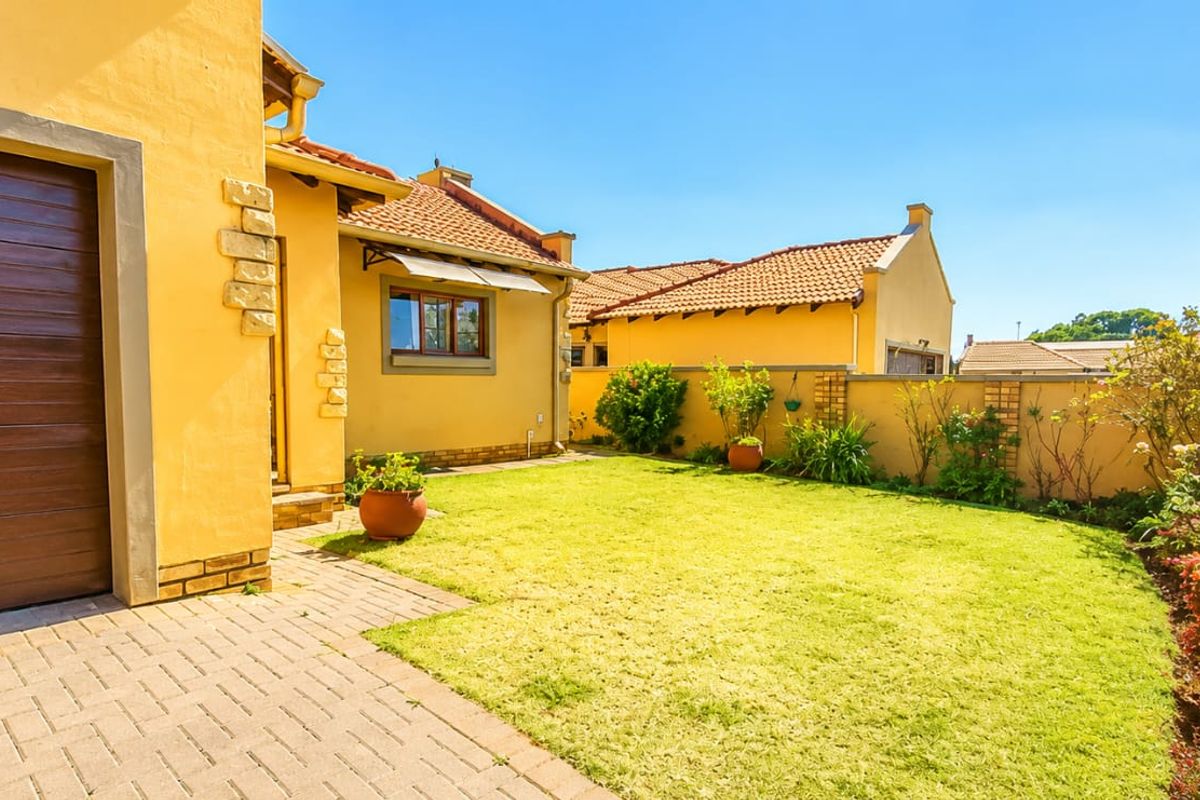A well-maintained rear exterior view featuring a paved driveway, a single garage, a neat lawn, and a secure boundary wall.