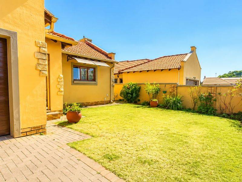 A well-maintained rear exterior view featuring a paved driveway, a single garage, a neat lawn, and a secure boundary wall.