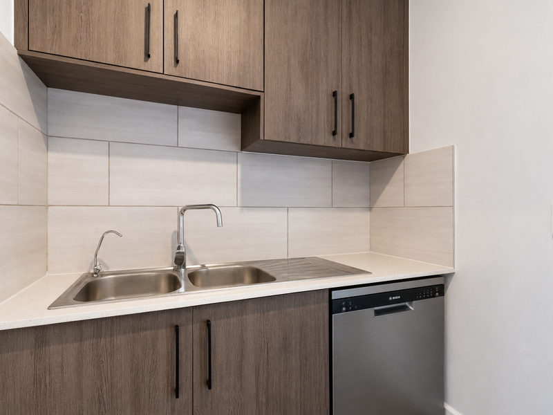 A modern, well-appointed scullery featuring sleek wood-grain cabinetry, stone benchtops, a double stainless steel sink, and an integrated dishwasher.