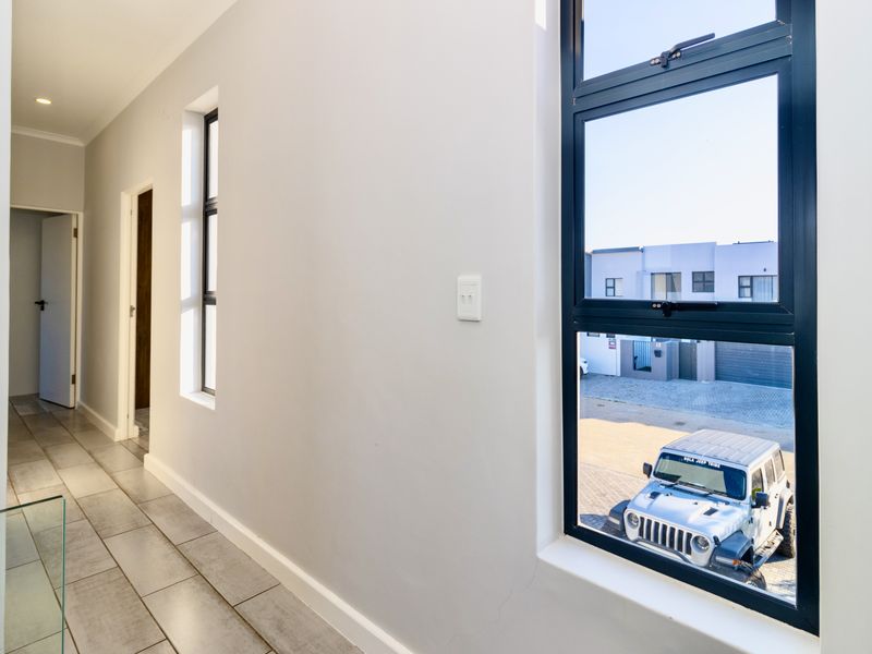 A bright, modern hallway featuring neutral wall finishes, tiled flooring, and large aluminium-framed windows providing natural light and a view of the exterior.