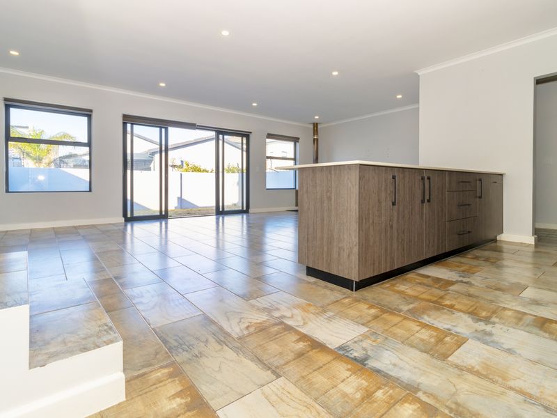 Spacious open-plan living area featuring modern tiled flooring, a central kitchen island with built-in cabinetry, and large sliding doors leading to the exterior.