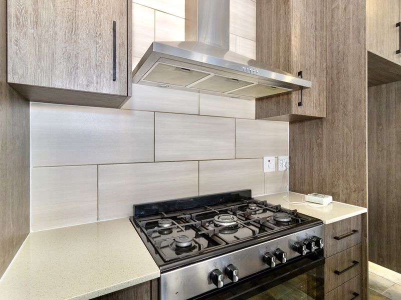Modern kitchen featuring wood-grain cabinetry, stone countertops, a tiled backsplash, and a stainless steel gas stove with an integrated extractor fan.