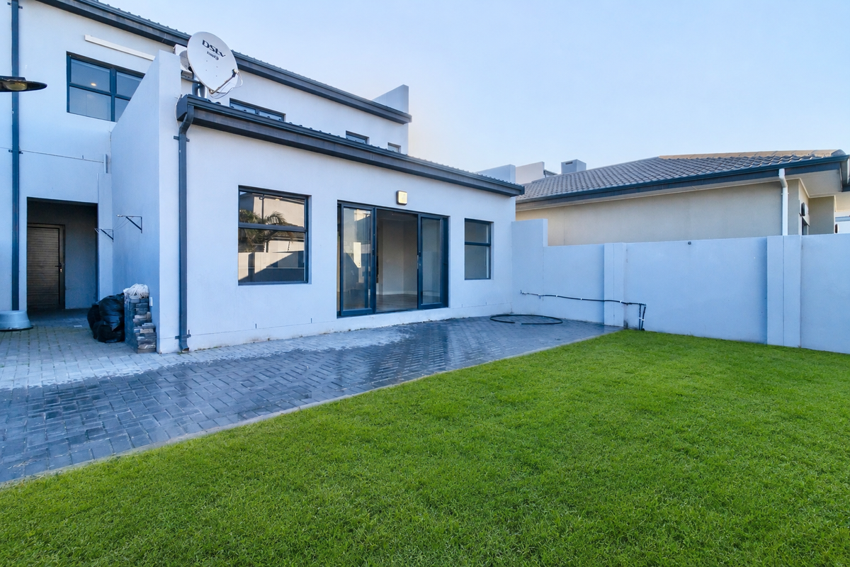 Rear view of the property featuring a paved patio area, a well-maintained lawn, and sliding glass doors leading into the home.