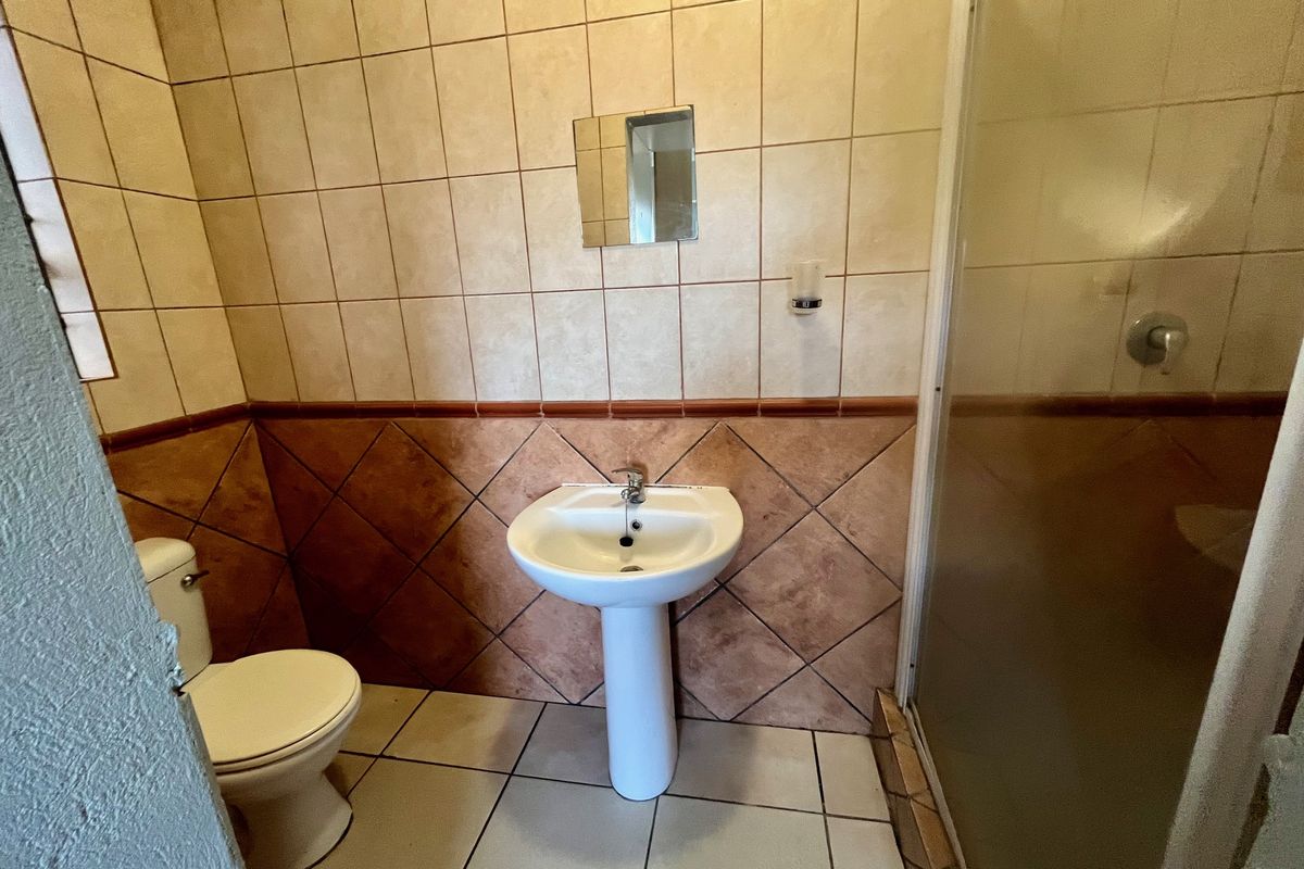 A functional bathroom featuring a pedestal basin, toilet, and shower enclosure with tiled walls and flooring, requiring cosmetic updates.